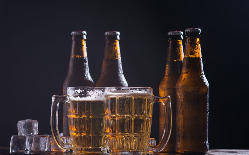Glass bottles of beer with glass and ice on dark background