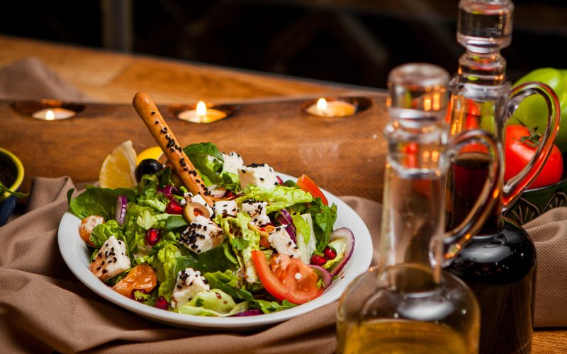 Side view greek salad with olive oil and soy sauce and candles in round white plate on table background